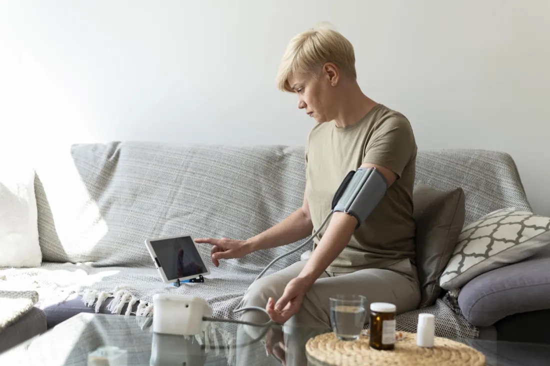 Woman using a home blood pressure monitor on a sofa.